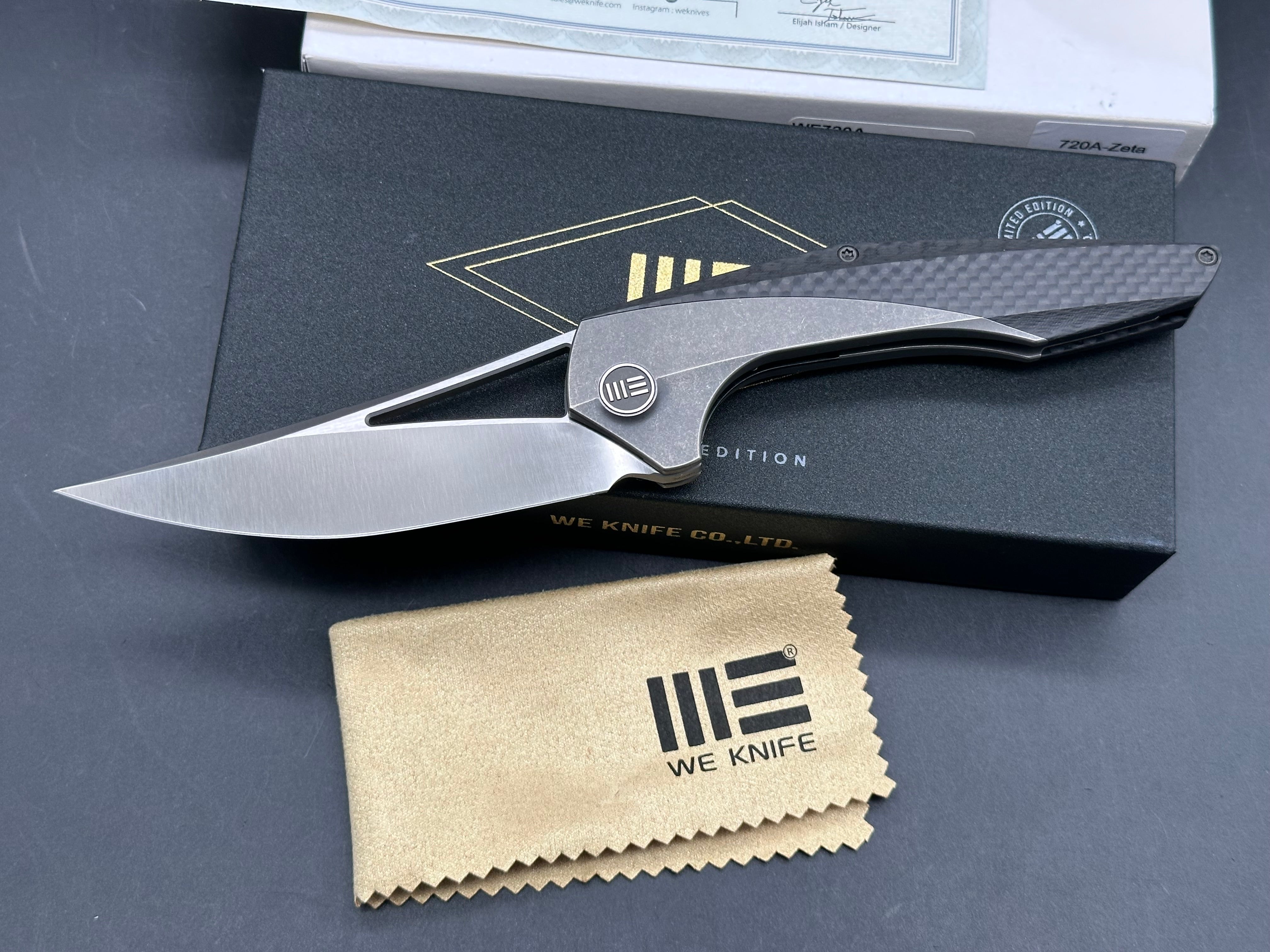 We Zeta: Elijah Isham design. 3.875 inch M390, trailing point, flat grind, satin finish blade. Frame lock. Carbon fiber and titanium handle