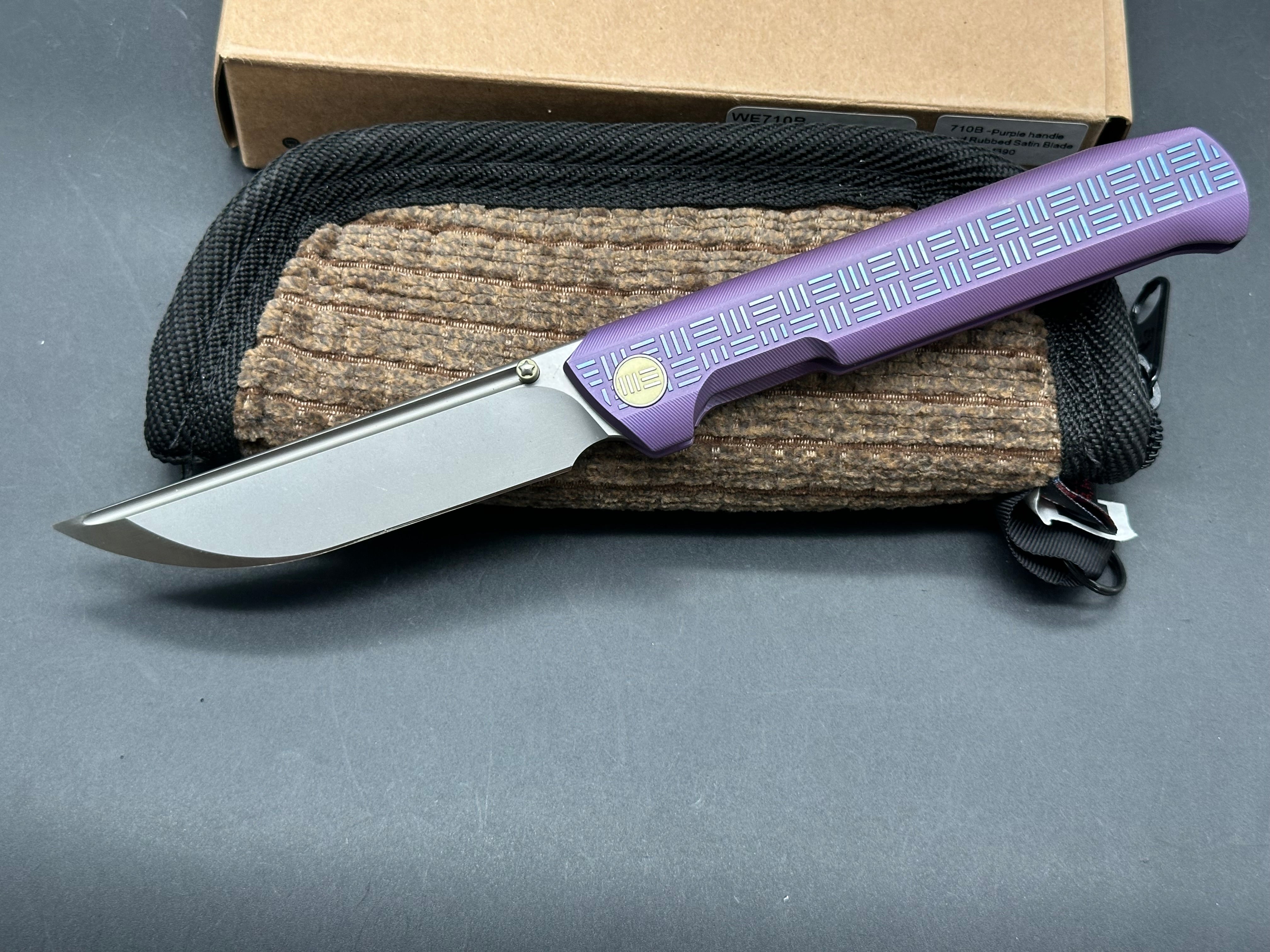 We 710B: 3.85 inch, flat grind, satin, M390 blade. Purple anodized handle. Frame lock. Ceramic bearings