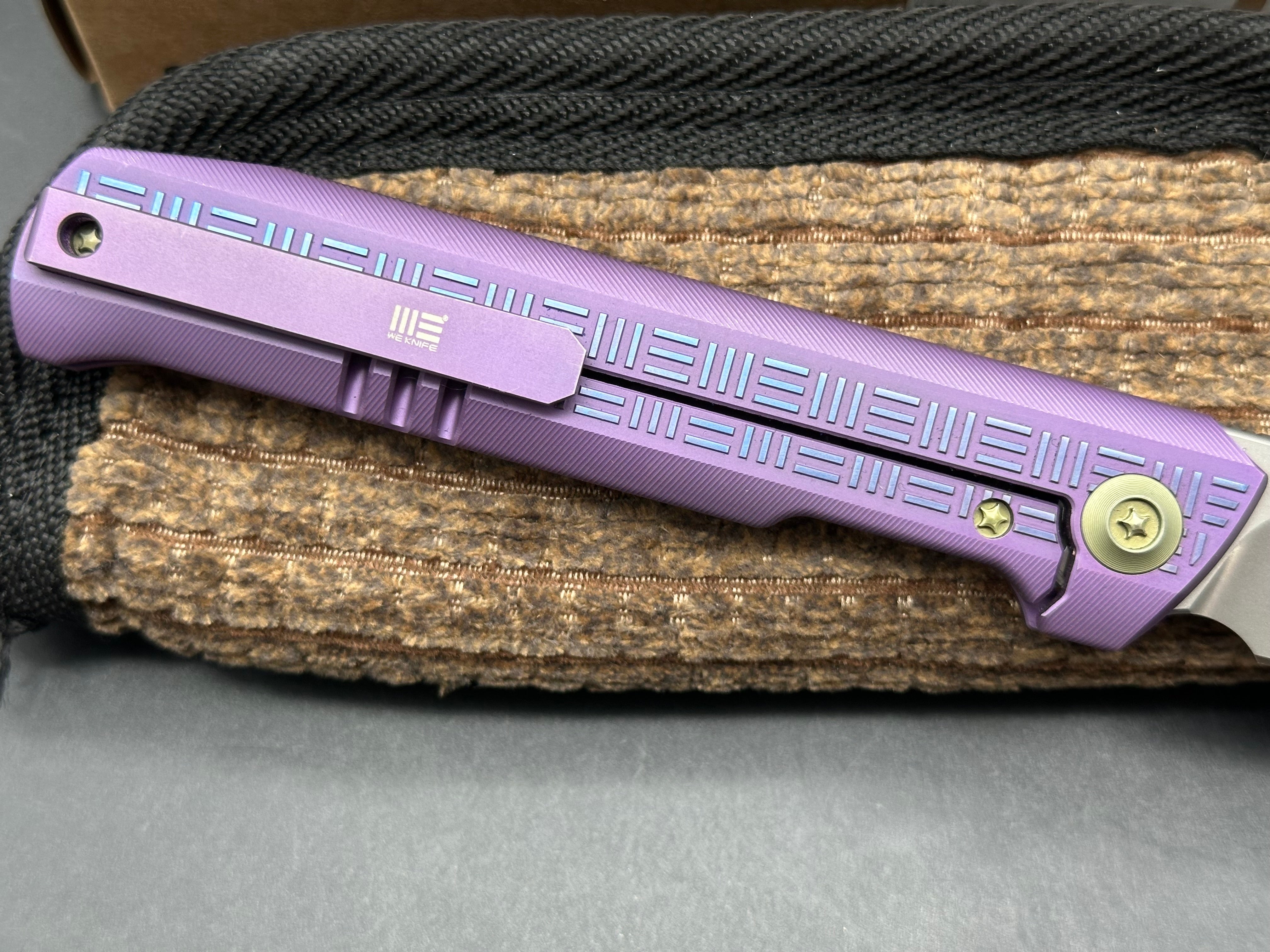 We 710B: 3.85 inch, flat grind, satin, M390 blade. Purple anodized handle. Frame lock. Ceramic bearings