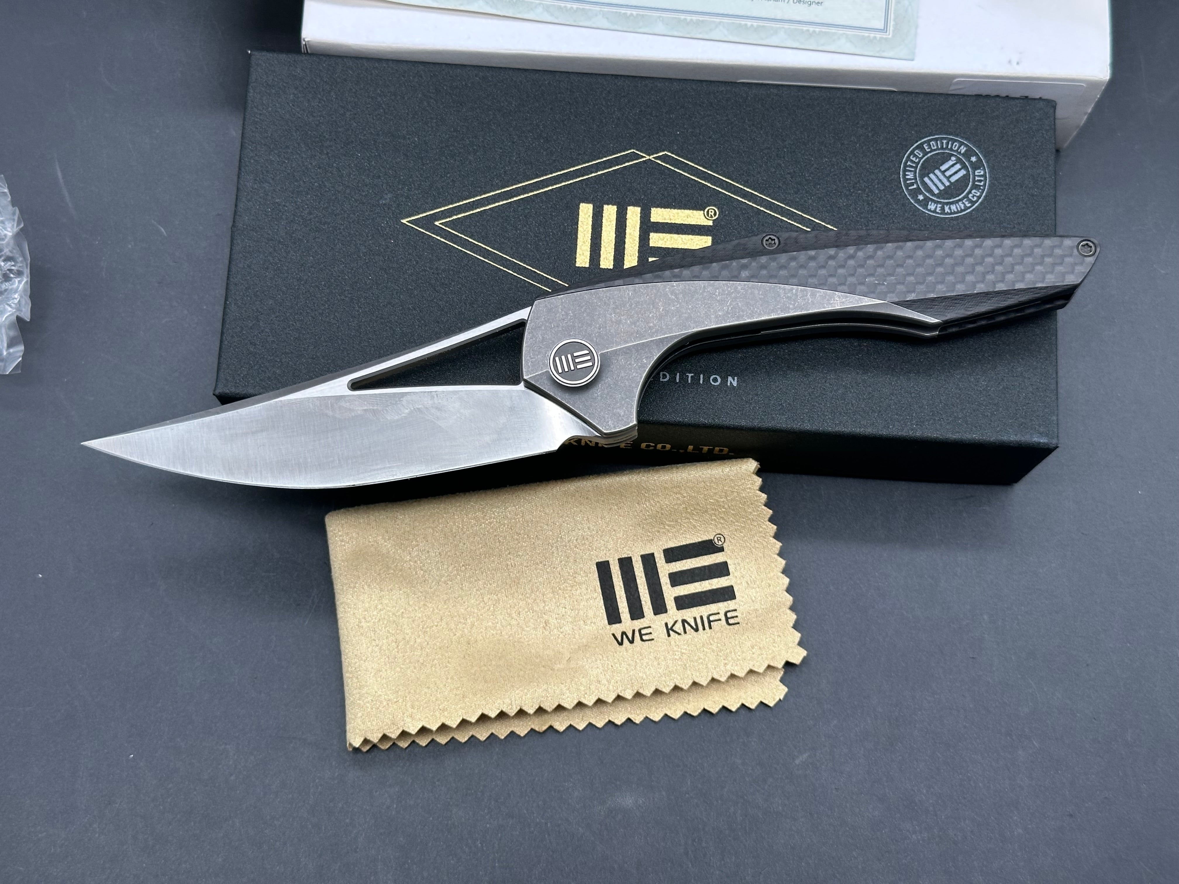We Zeta: Elijah Isham design. 3.875 inch M390, trailing point, flat grind, satin finish blade. Frame lock. Carbon fiber and titanium handle