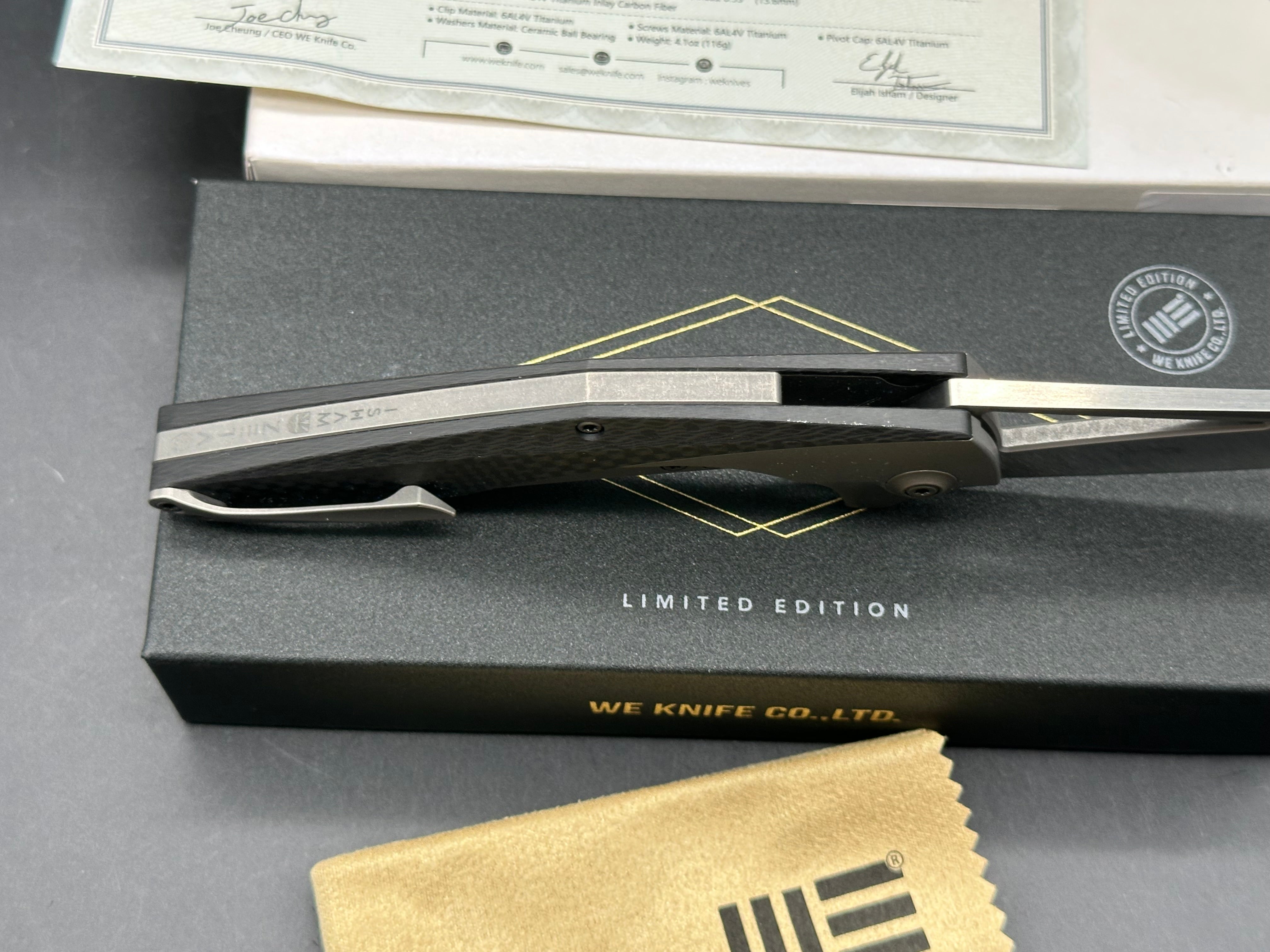 We Zeta: Elijah Isham design. 3.875 inch M390, trailing point, flat grind, satin finish blade. Frame lock. Carbon fiber and titanium handle