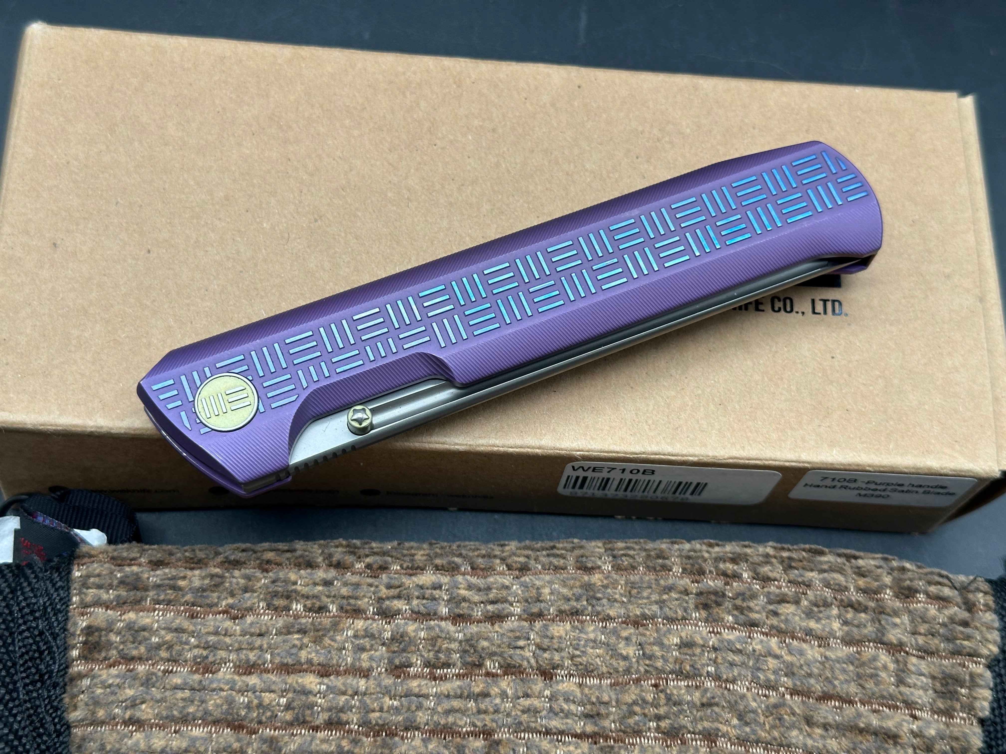 We 710B: 3.85 inch, flat grind, satin, M390 blade. Purple anodized handle. Frame lock. Ceramic bearings