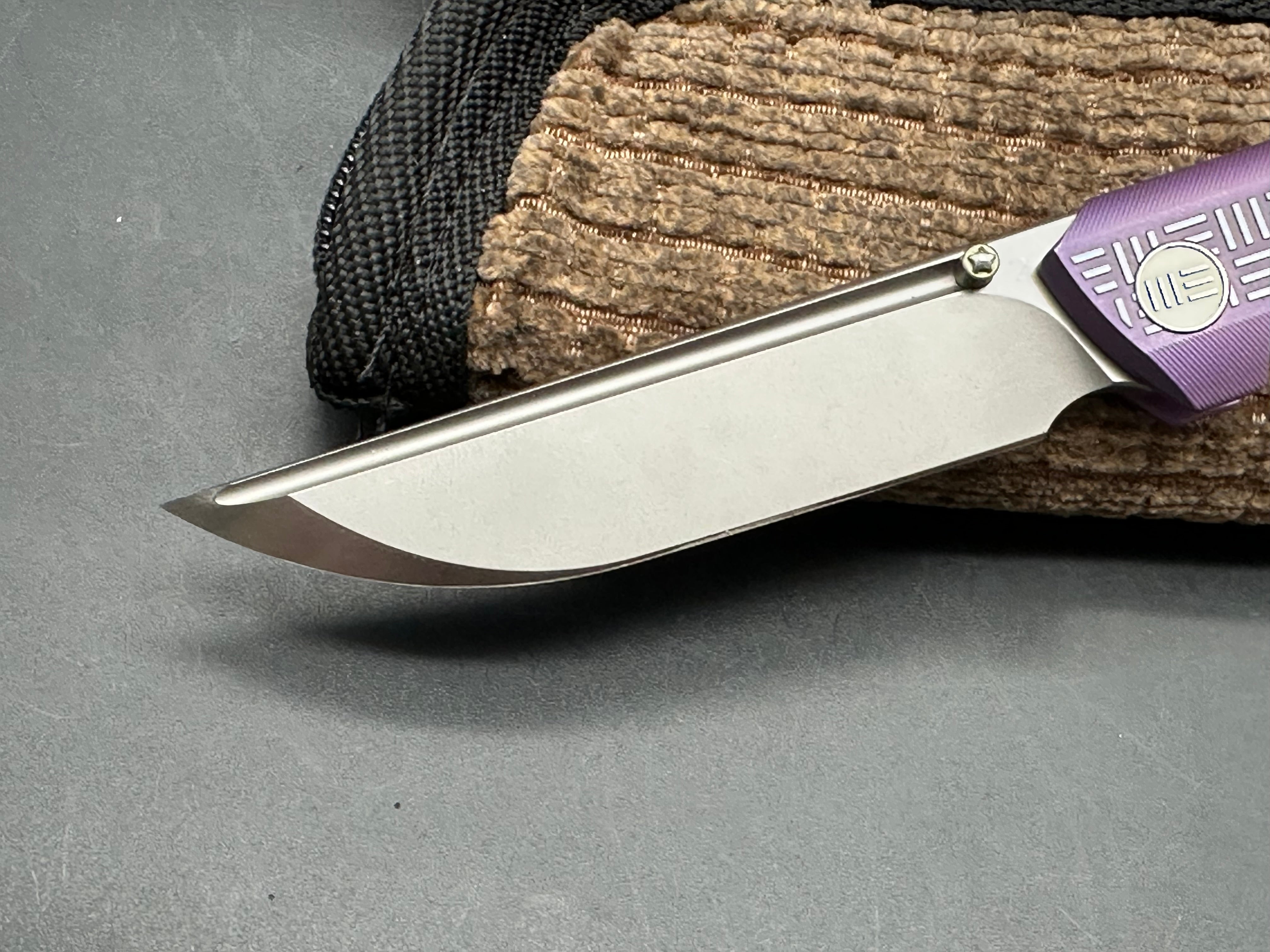 We 710B: 3.85 inch, flat grind, satin, M390 blade. Purple anodized handle. Frame lock. Ceramic bearings