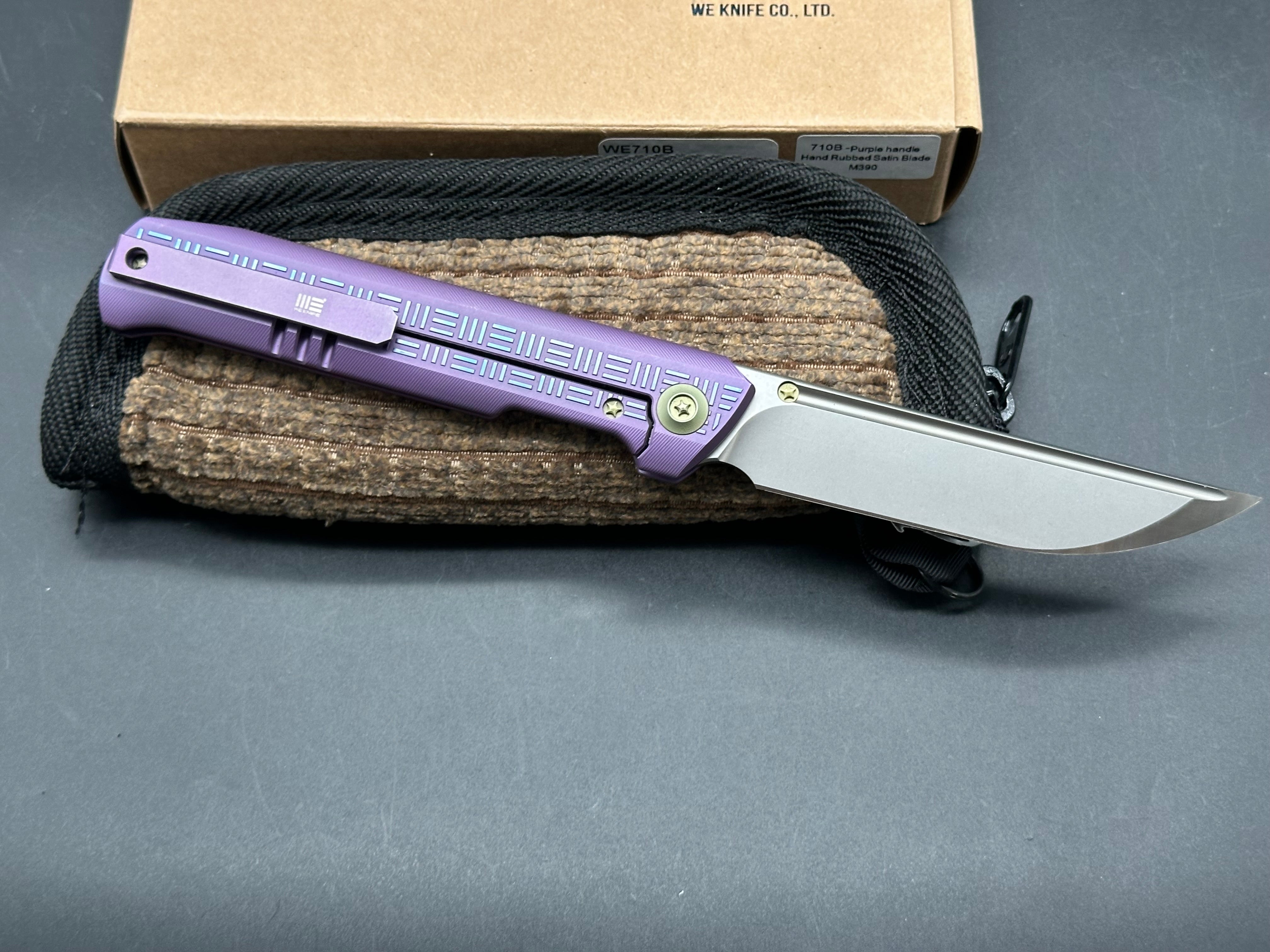 We 710B: 3.85 inch, flat grind, satin, M390 blade. Purple anodized handle. Frame lock. Ceramic bearings