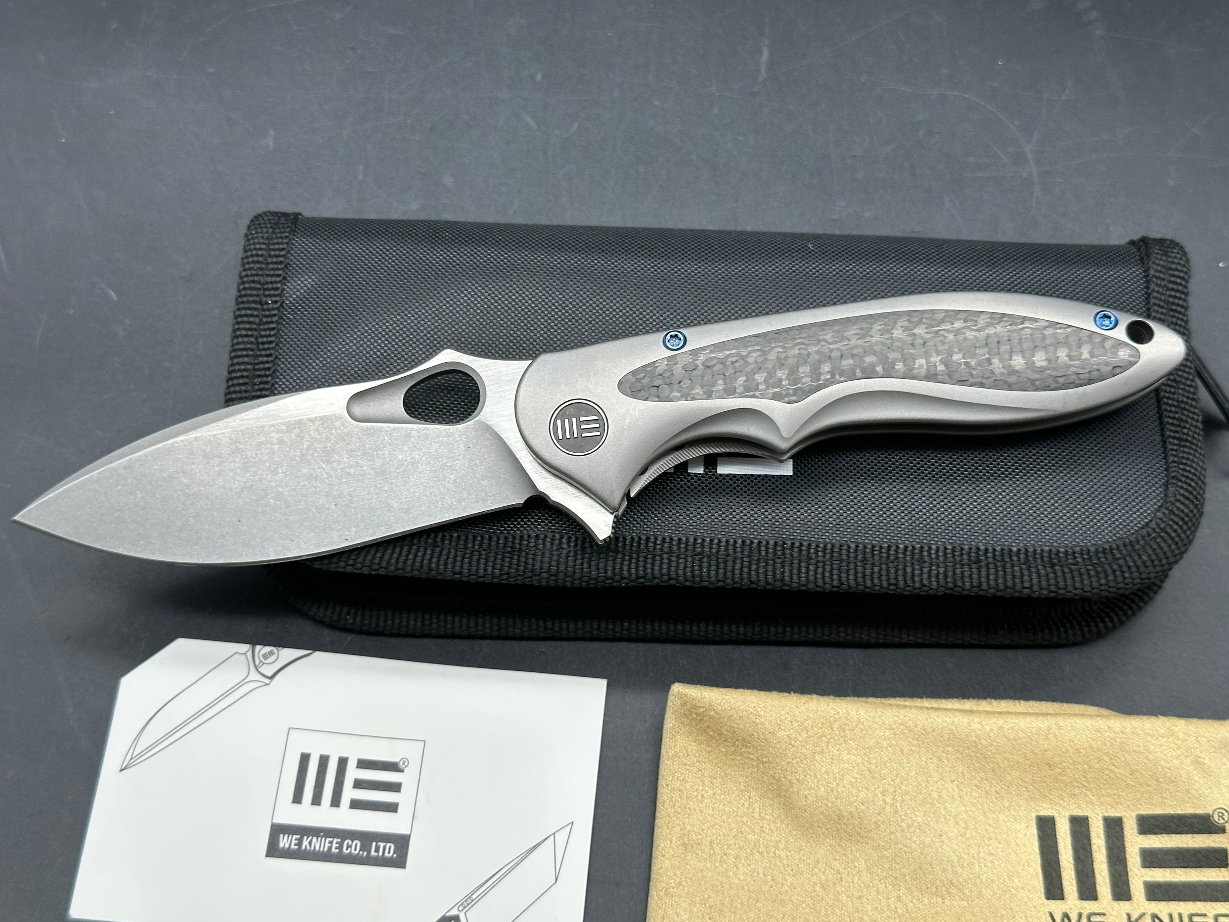 We Knives Zephyr: 3.5 inch drop point, flat grind, Bohler M390 blade. Titanium handle with carbon fiber inset