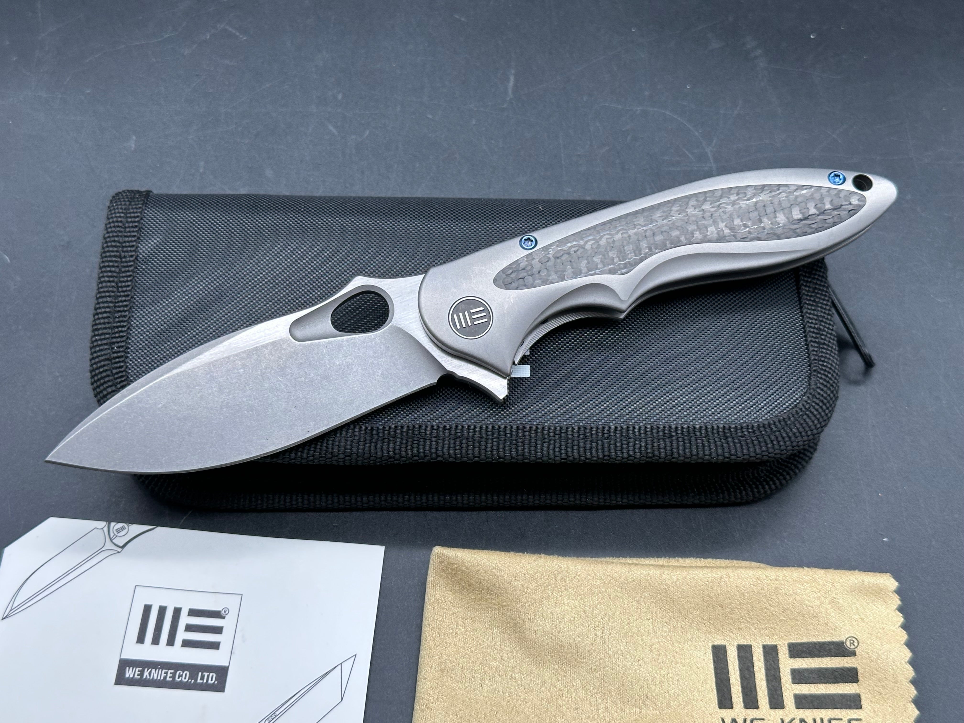 We Knives Zephyr: 3.5 inch drop point, flat grind, Bohler M390 blade. Titanium handle with carbon fiber inset